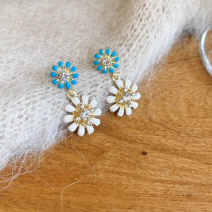 Detailed close-up of daisy floral earrings with blue and white petals on soft fabric