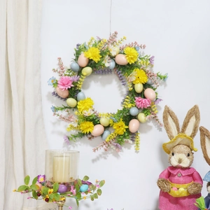 Easter wreath with pastel eggs and faux flowers hung on white wall with festive decor