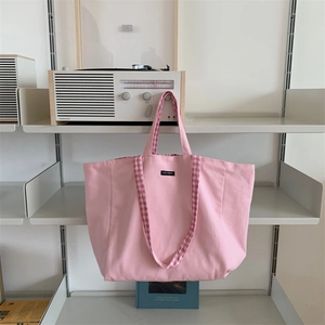 Detailed shot of pink canvas tote bag with plaid handles and black woven brand label