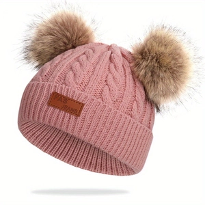 Détail du bonnet en tricot rose pour enfant avec deux pompons marron et écusson en cuir