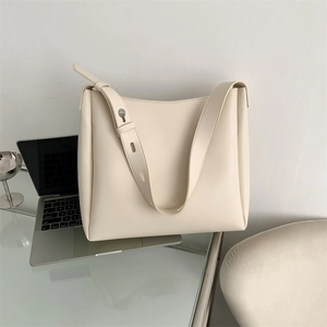 Detailed texture of cream white leather tote bag on a glass table with laptop and glass