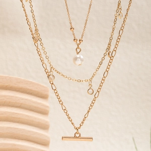 Detail of layered gold necklace featuring faux pearl, rhinestone and bar pendant charms