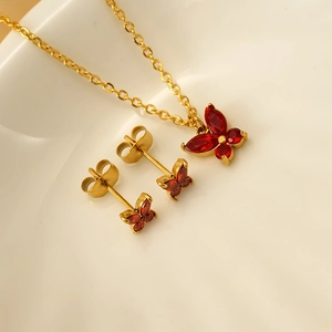 Goldenes Schmetterling Schmuckset mit roten Zirkonia Steinen auf Keramikteller