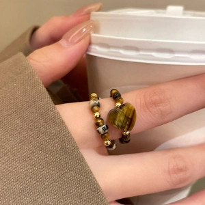 Macro shot of tiger eye heart stone beaded elastic ring with gold accents on finger