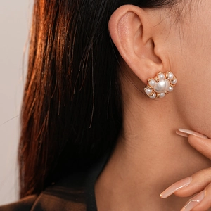 Close-up of a model wearing pearl flower stud earrings with a gold-plated finish