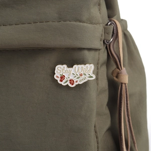 Macro shot of Stay Wild enamel pin with red flowers on green canvas backpack