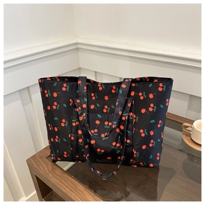 Detail of black tote bag with red cherry prints on a glossy nylon fabric surface