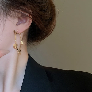 Detailed view of large gold hoop earring with delicate butterfly charm on model