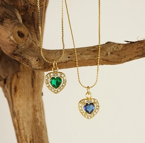 Close-up of gold twist chain necklaces featuring green and blue heart zircon pendants on wood