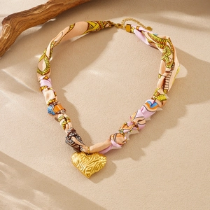 Detailed view of scarf choker necklace with textured gold heart pendant and print fabric
