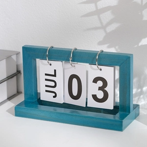 Minimalist blue wooden flip calendar with white date cards on desktop with plant shadow