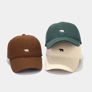 Detail of embroidered polar bear logo on brown, dark green, and beige cotton baseball caps