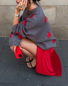 Close-up of grey knit sweater with red heart pattern paired with red satin skirt