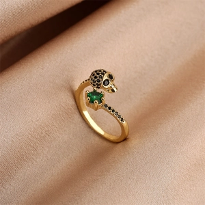 Macro shot of gothic gold skull ring with black micro-pave and green stone on silk