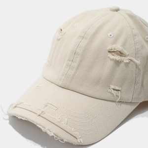 Detail view of beige distressed cotton baseball cap showing ripped edges and vintage fabric texture