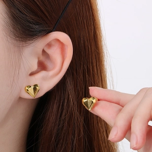 Close-up of 18k gold plated heart stud earrings worn on ear showing faceted metal detail
