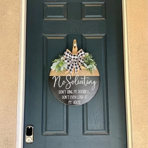 Close-up of wooden No Soliciting front door sign with buffalo plaid bow and greenery