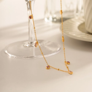 Collier en acier doré avec des pierres roses rondes et rectangulaires sur table blanche