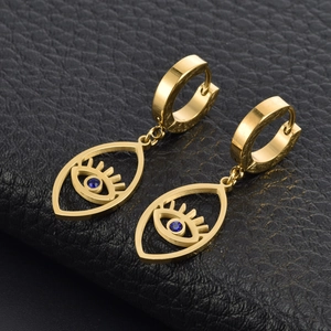 Detailed close-up of golden evil eye earrings with blue crystals on black leather