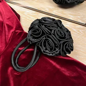 Close-up of black satin handbag featuring 3D handmade roses on red velvet fabric
