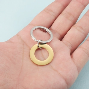 Hand holding a minimalist golden circle pendant with silver keychain on blue paper