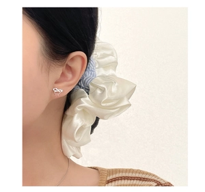 Close-up of elegant S999 silver bow earrings worn with a white satin hair tie on a model