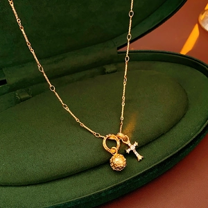 Dettaglio collana con croce dorata e ciondolo a sfera in una scatola di velluto verde