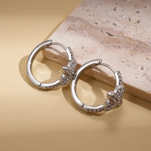 Macro shot of silver bear hoop earrings with zircon pavé on natural stone texture