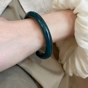 Detail of dark green resin bangle with natural texture on beige suit sleeve