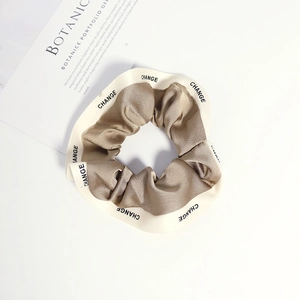 Close-up of a satin scrunchie with CHANGE lettering next to an aesthetic book