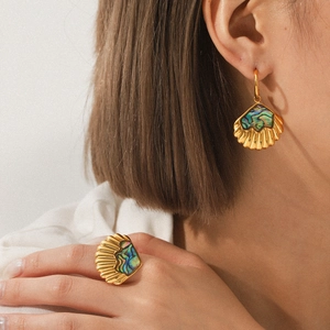 Close-up of golden shell-shaped earrings and ring set with abalone shell inlay