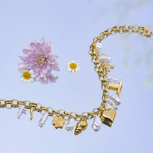 Gros plan d'un collier doré avec perles et breloques cœur sur une surface réfléchissante