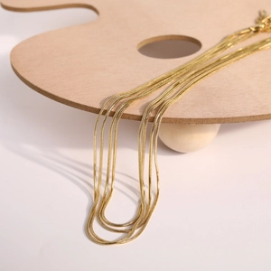 Detail of 18K gold-plated titanium snake bone chain necklaces layered on wooden display
