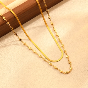 Détail d'un collier double épaisseur doré avec breloques cœur et étoile sur support en bois
