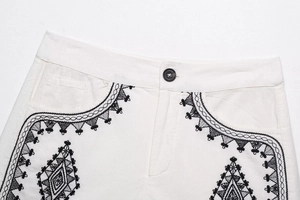 Detail of white cotton shorts featuring intricate black ethnic embroidery and button closure
