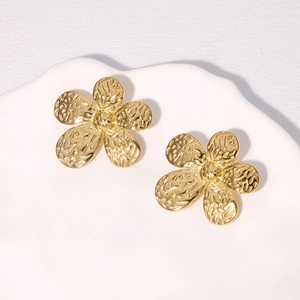 Elegant gold flower stud earrings with hammered texture on a white ceramic tray