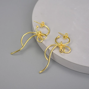 Elegant gold bow ribbon earrings with polished finish on a grey geometric base