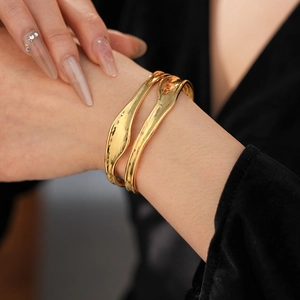 Detail of gold open bangles featuring irregular lava texture and double-layer fluid design