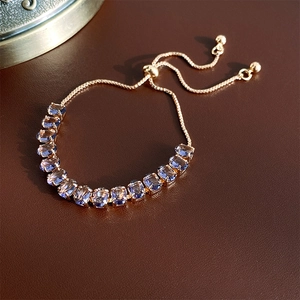 Detail of adjustable gold bolo bracelet with purple oval-cut zircon on brown leather background