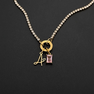 Detail view of a gold-plated titanium steel necklace with letter A and pink gemstone charm