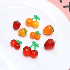Detail shot of strawberry and cherry resin charms with metal loops on a white plate
