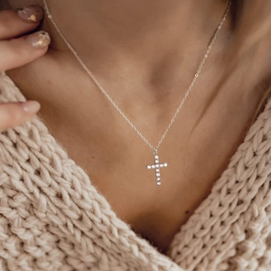 Detail of cross pendant necklace with clear cubic zirconia on a beige knit sweater