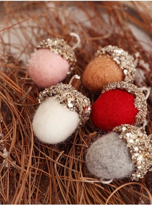 Detailed view of handmade wool felt acorn ornaments with sequins on pine needles background