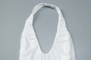 Close-up detail of white halter neck dress with pleated V-neck and smooth fabric texture