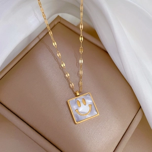 Close-up of gold square necklace featuring a white shell inlay and happy smiley face detail