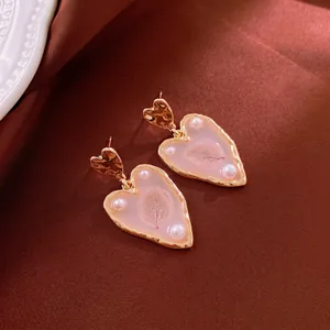 Gold plated heart earrings with pearls and dried flowers on brown silk fabric
