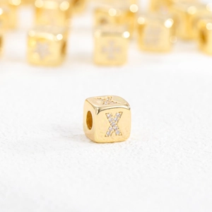 Macro shot of 18k gold cube pendant with sparkling zircon inlaid letter X design