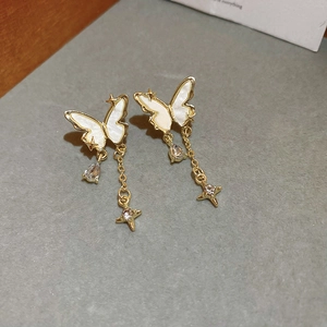 Détail de boucles d'oreilles papillon dorées avec nacre blanche et pendentifs étoile