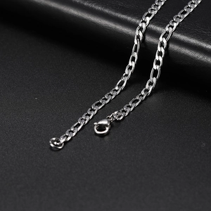 Detail shot of a silver Figaro chain with a lobster clasp on a black leather surface