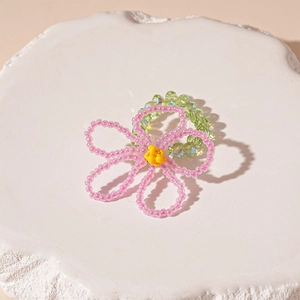 Close-up of handmade pink glass flower ring on white textured stone with green beads